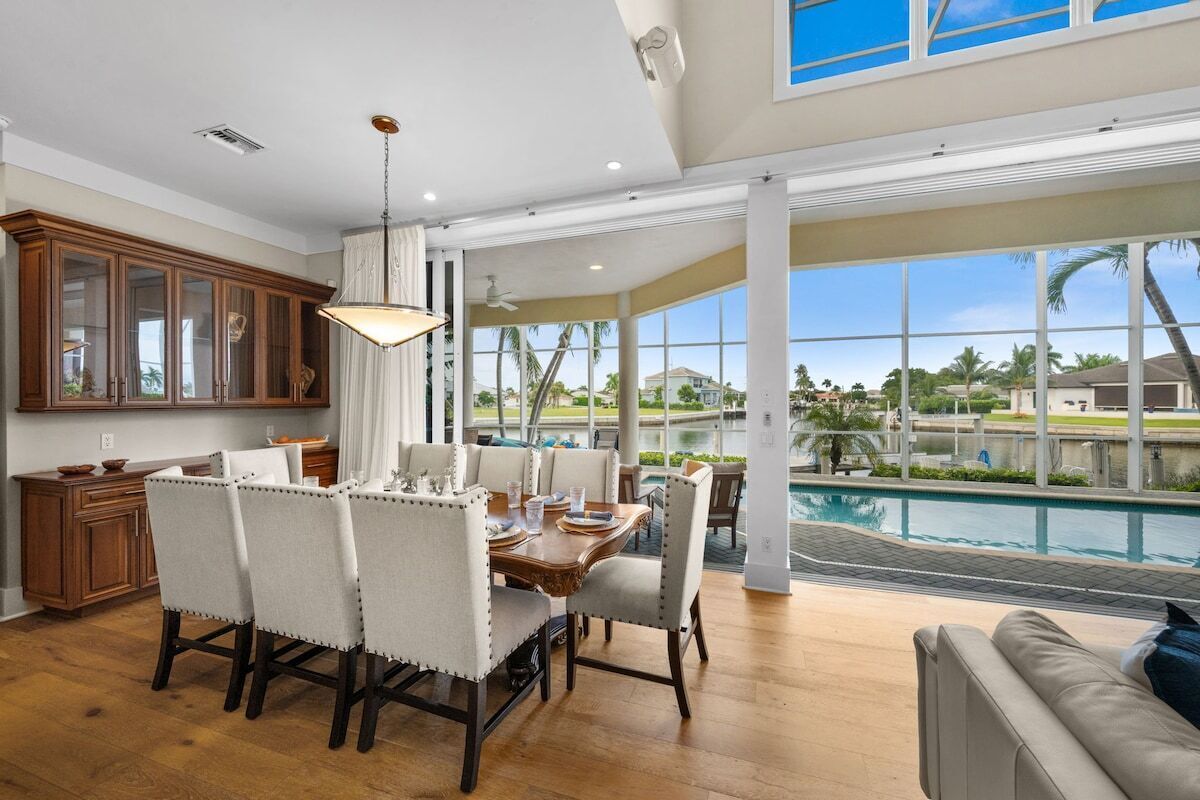 A spacious dining area with a view of a swimming pool and palm trees.