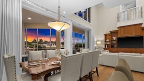 A dining area with a table set for four, a large window with a view, and a modern entertainment center. - Waterfront Estate • Rooftop • Heated Pool/Spa (Marco Island)
