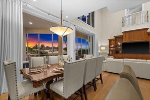 A dining area with a table set for four, a large window with a view, and a modern entertainment center. - Waterfront Estate • Rooftop • Heated Pool/Spa (Marco Island)