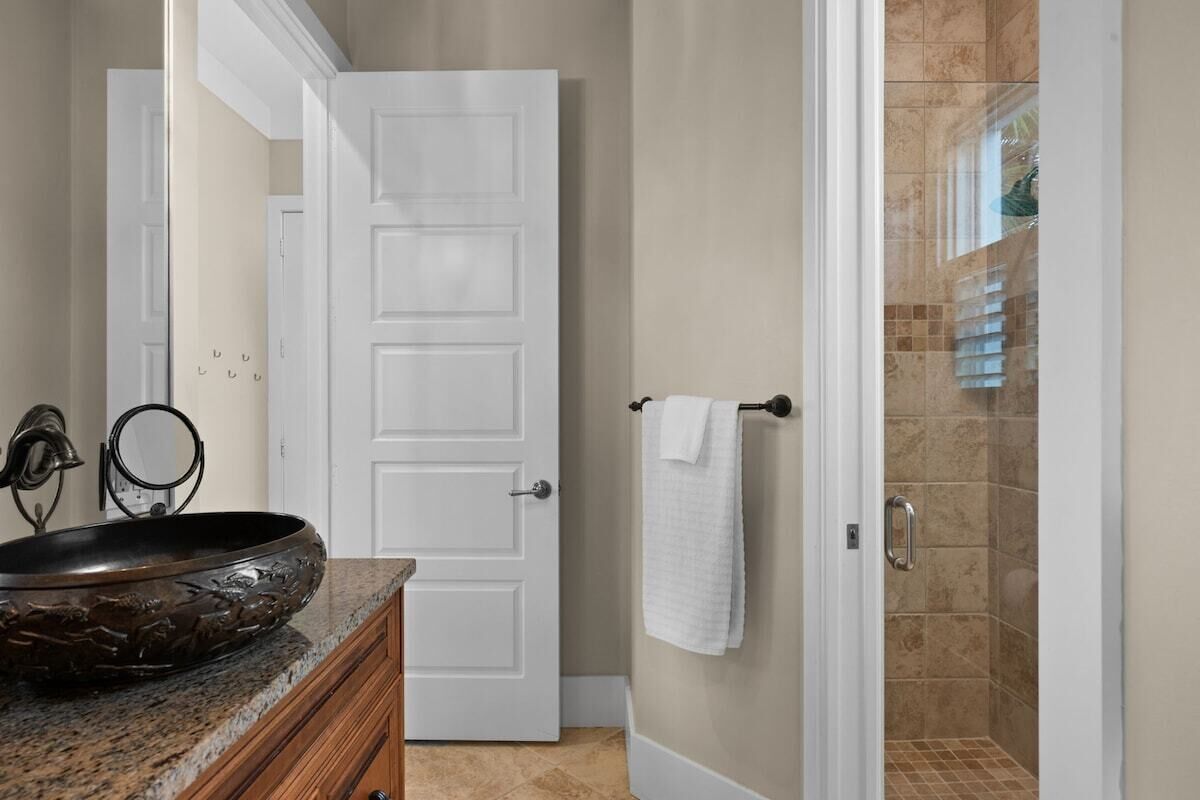 A bathroom with a granite countertop, a white door, and a shower area.