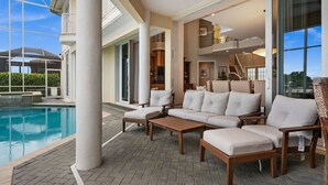 A poolside area with a sectional sofa, a wooden table, and a glass-enclosed space. - Waterfront Estate • Rooftop • Heated Pool/Spa (Marco Island)