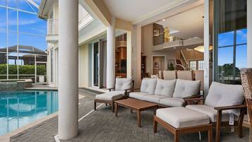 A poolside area with a sectional sofa, a wooden table, and a glass-enclosed space.