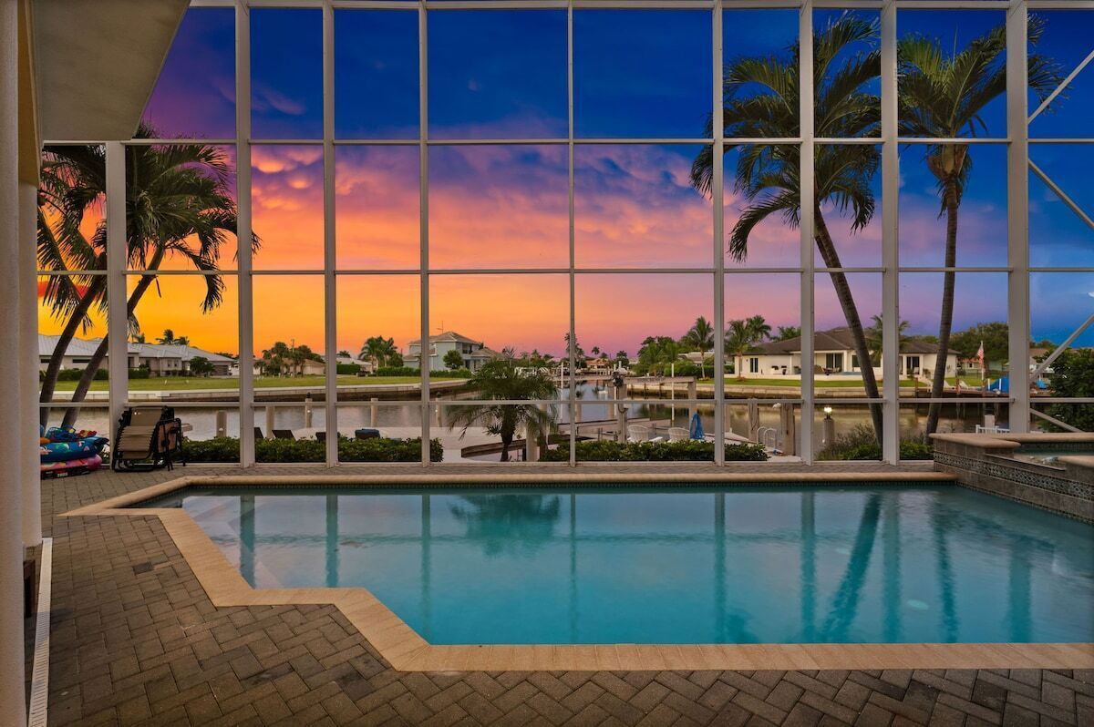 Une piscine intérieure avec vue sur des palmiers et un coucher de soleil.