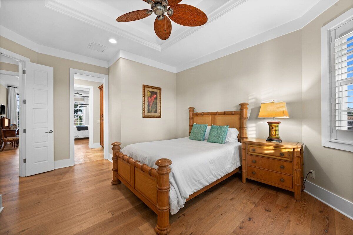 A bedroom with a wooden bed, a nightstand with a lamp, a ceiling fan, and a door leading to another room.