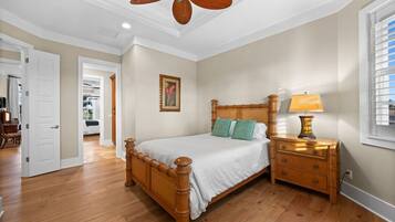 A bedroom with a wooden bed, a nightstand with a lamp, a ceiling fan, and a door leading to another room.