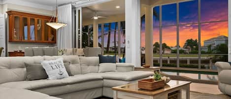 A modern living room with a sectional sofa, a coffee table, and a large window with a sunset view.