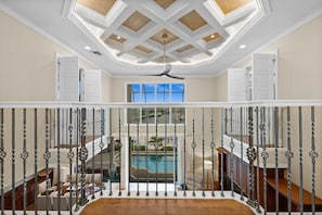 A spacious interior with a high ceiling, a central pool view, and a modern staircase with metal railings. - Waterfront Estate • Rooftop • Heated Pool/Spa (Marco Island)
