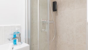 Een badkamer met een douchecabine van glas, een wit wastafelmeubel met zeepdispenser en een spiegel.
