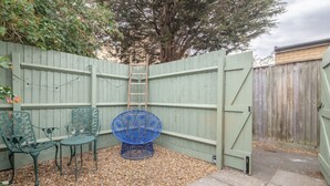 Een omheind buitengebied met een houten poort, een blauwe stoel en een metalen tafel.