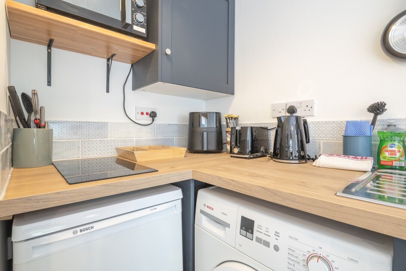 A compact kitchen with a Bosch dishwasher, a coffee maker, and a kettle on the counter.