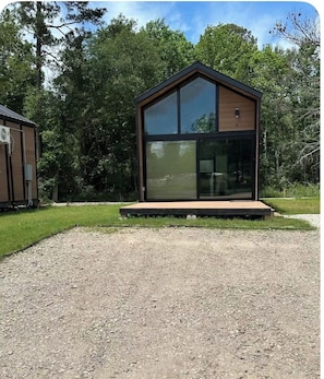 A modern building with a large glass window, a wooden deck, and a gravel driveway.