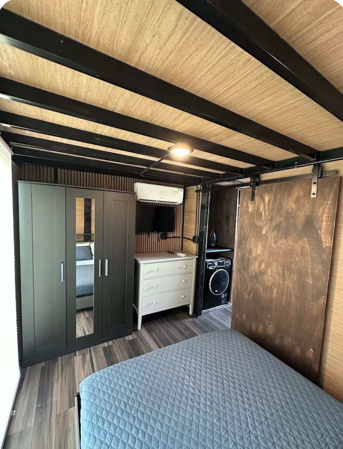 A compact room with a bed, wardrobe, and a washing machine.
