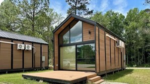 A modern wooden cabin with a large glass window, a wooden deck, and a metal roof.