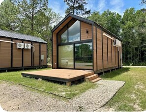 A modern wooden cabin with a large glass window, a wooden deck, and a metal roof.