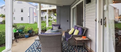 A covered porch with outdoor furniture, a patterned rug, and a view of the neighborhood.