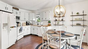 A modern kitchen with white cabinetry, a central island, and a chandelier. - Waterfront Condo | King Bed | Walk to Douglas (Douglas)