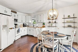 A modern kitchen with white cabinetry, a central island, and a chandelier. - Waterfront Condo | King Bed | Walk to Douglas (Douglas)