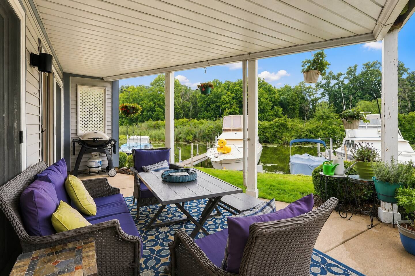 A covered patio with outdoor furniture, a table, and potted plants.