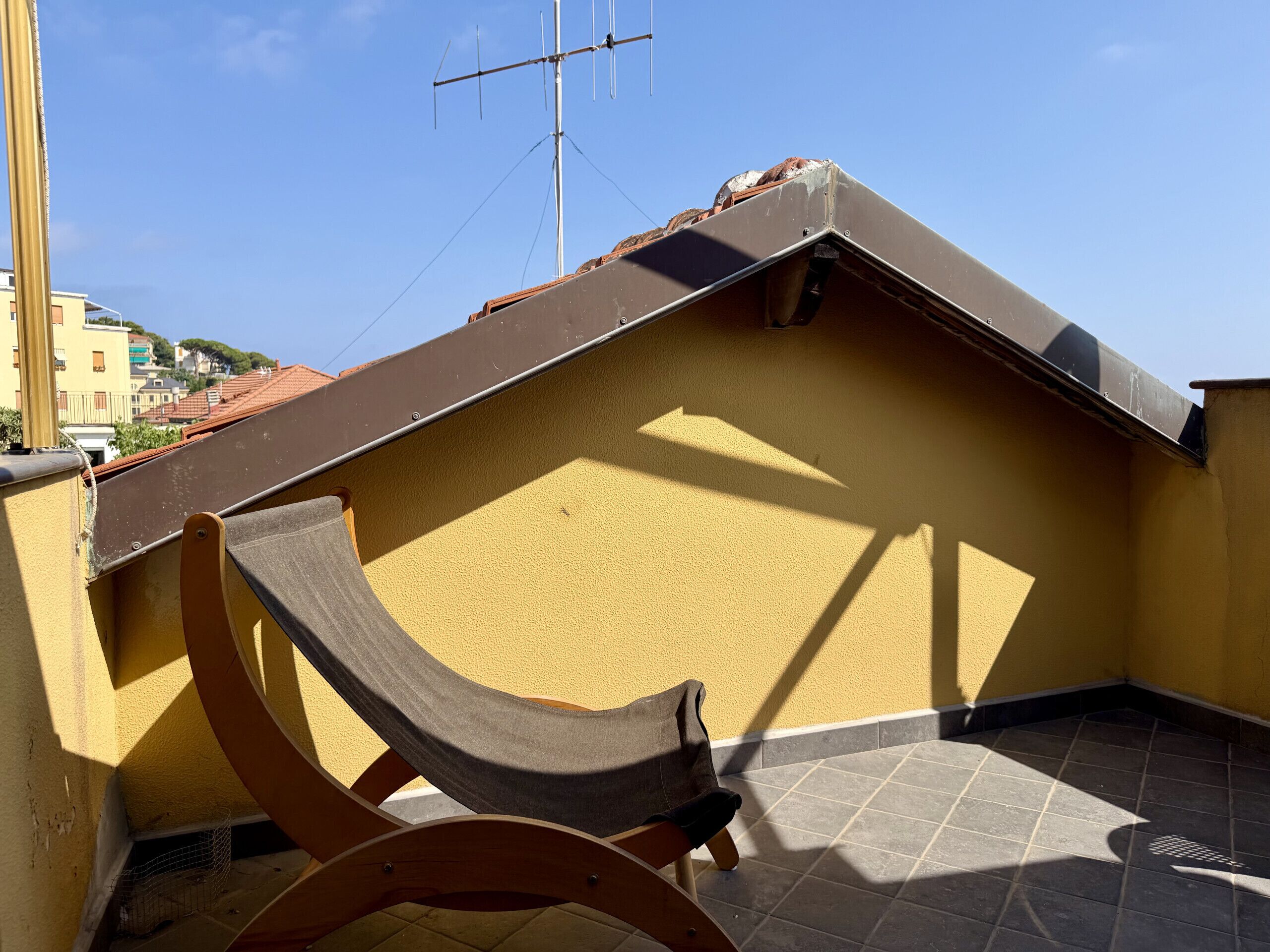 A rooftop terrace with a hammock, a tiled floor, and a view of buildings in the background.