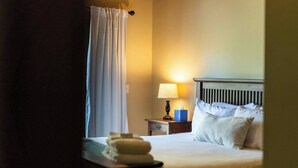 A hotel room with a bed, a nightstand with a lamp, a blue tissue box, and a window with a curtain.