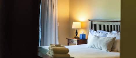 A hotel room with a bed, a nightstand with a lamp, a blue tissue box, and a window with a curtain.