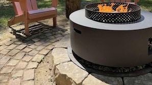 A circular fire pit with a metal frame and a flat top, surrounded by a stone border.