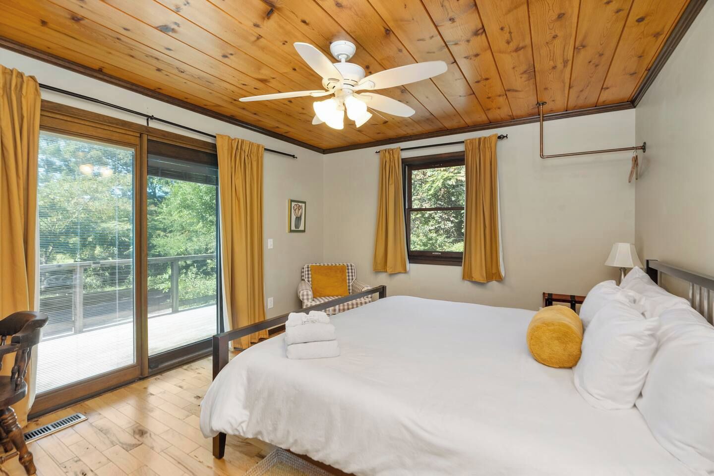 Un dormitorio con cama, ventilador de techo, ventana con cortinas y vista a zonas verdes.