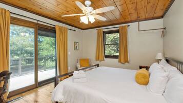 Un dormitorio con cama, ventilador de techo, ventana con cortinas y vista a zonas verdes.