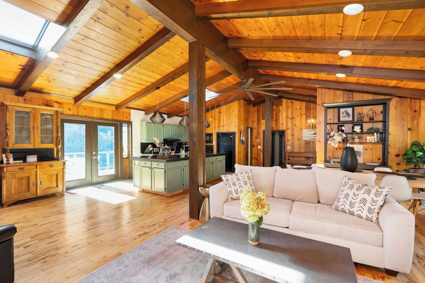 Amplia sala de estar con techo de madera, un sofá, una mesa de centro y una cocina al fondo.