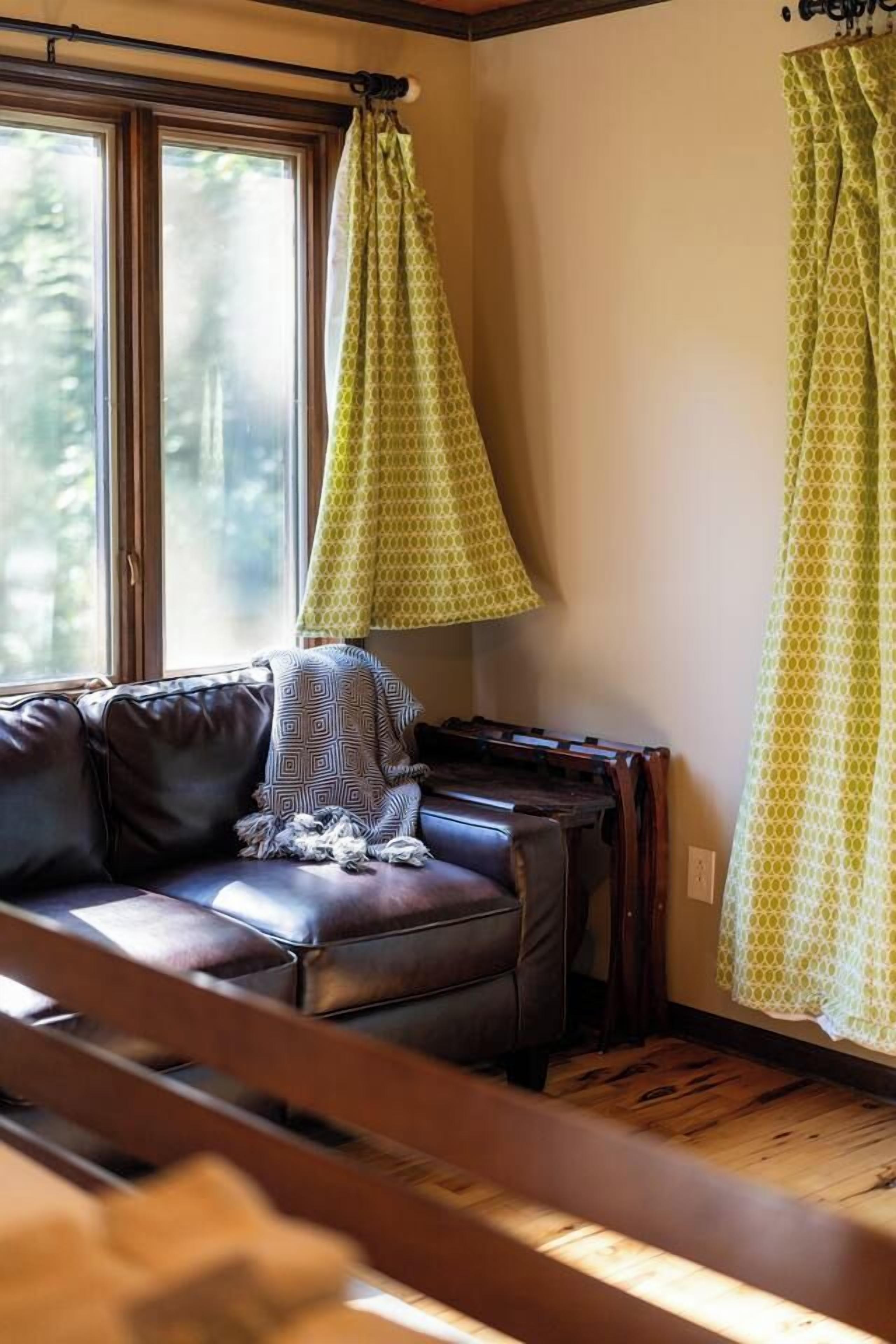 A room with a brown leather sofa, a wooden bench, and a window with curtains.