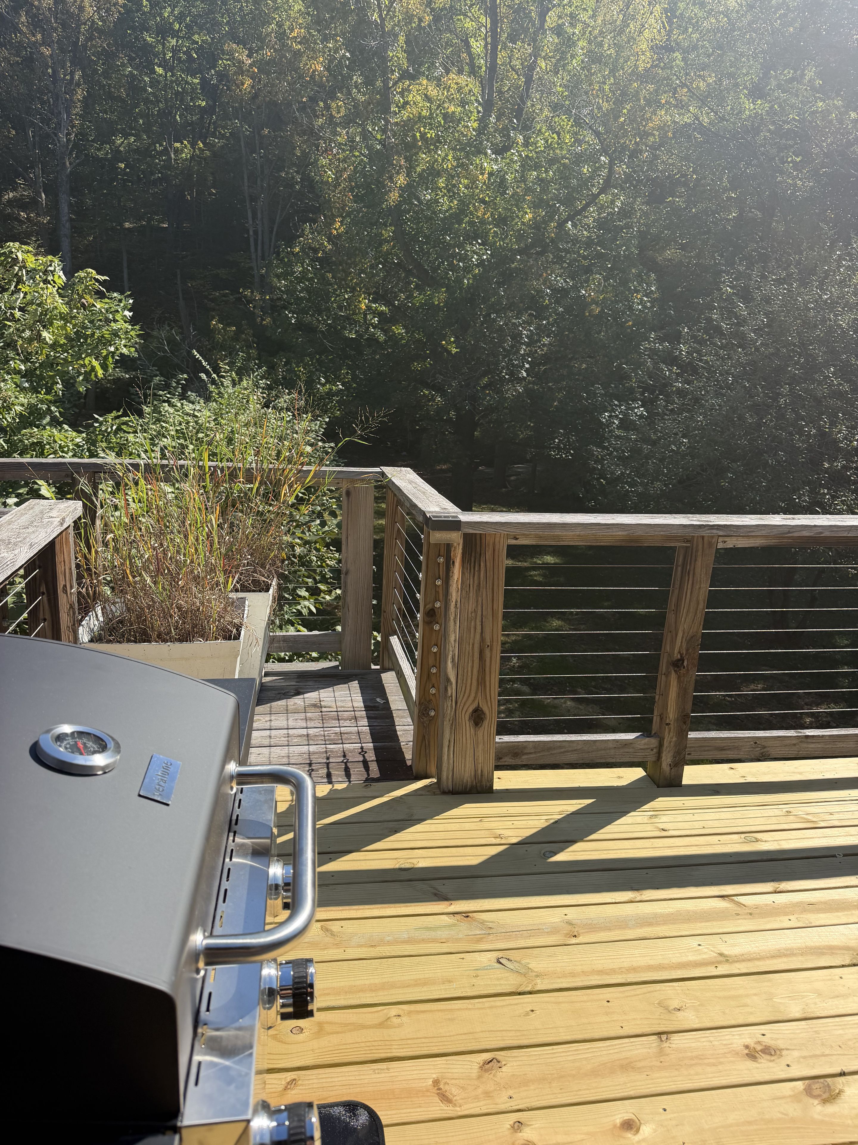A wooden deck with a barbecue grill, surrounded by trees.