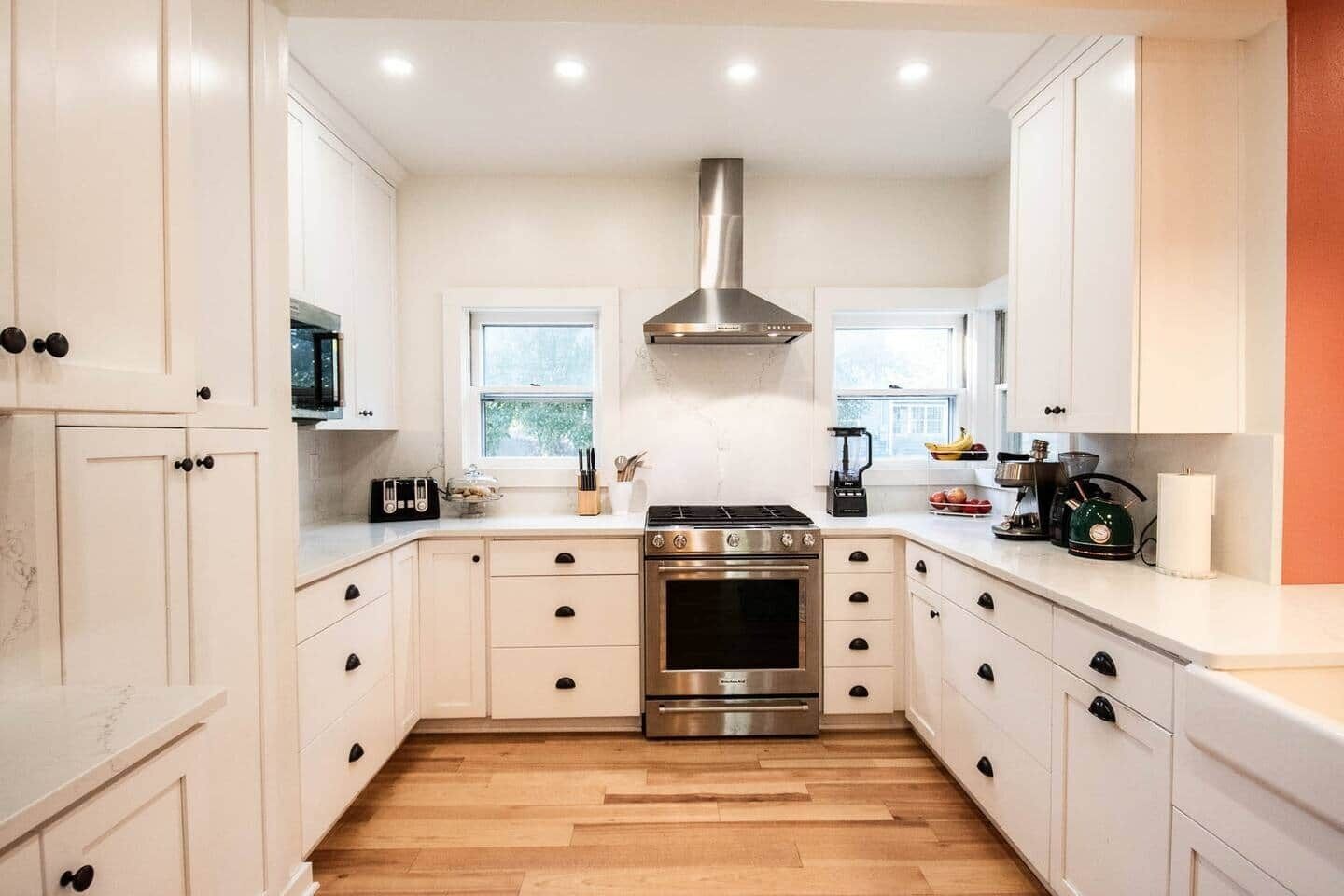 Une cuisine moderne avec des armoires blanches, une hotte en acier inoxydable et un plancher en bois.