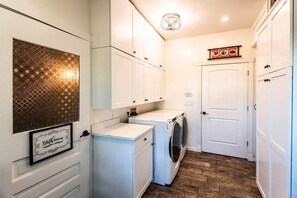 A compact laundry room with a washing machine, dryer, and a framed sign on the wall.