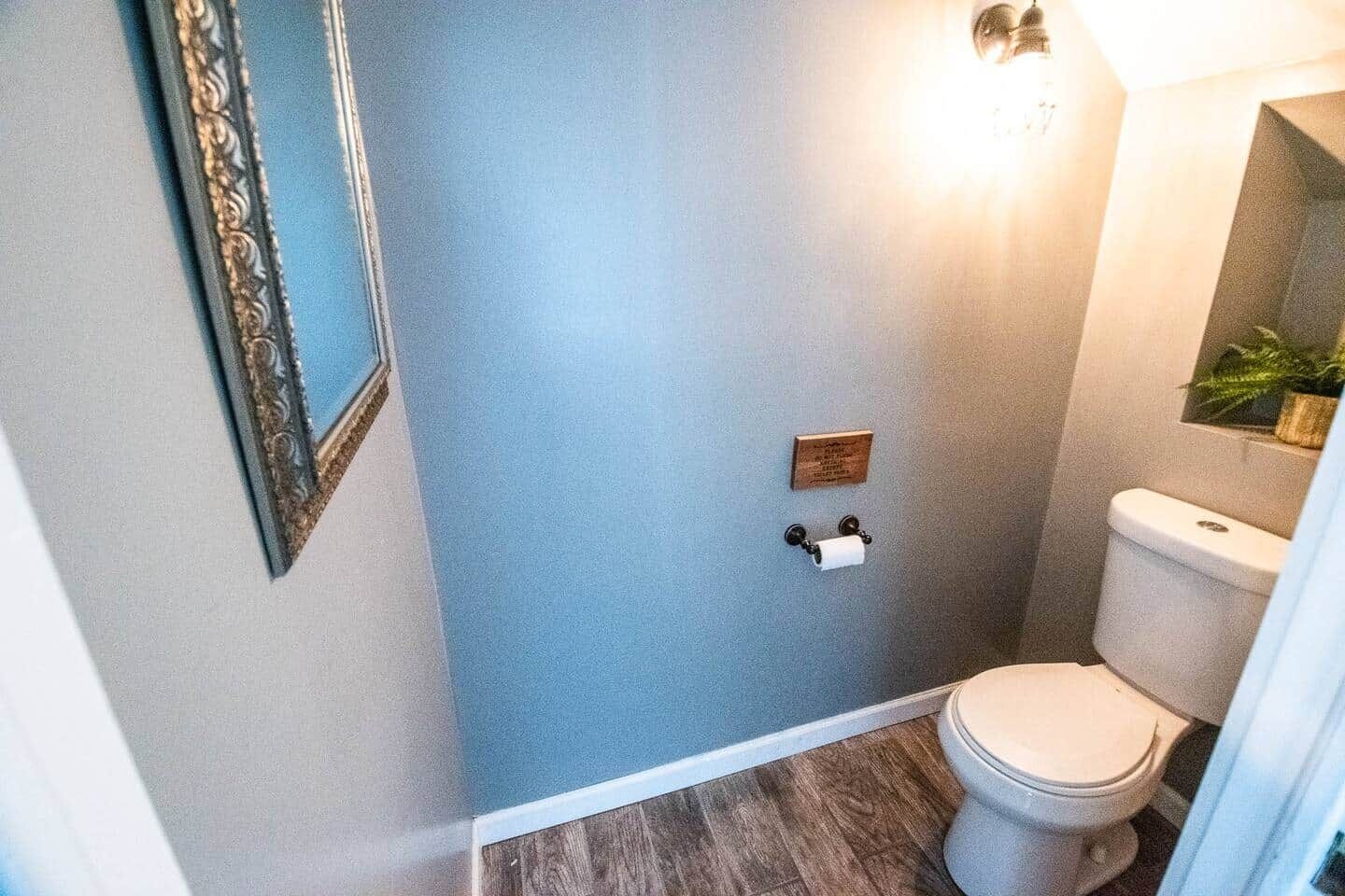 Ett badrum med en toalett, en spegel som är monterad på väggen och en lampa.