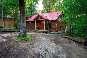 A log cabin with a red roof, surrounded by trees, and a gravel driveway leading to the entrance. - Rosebud | Hot Tub | WiFi | 2 Min Gorge Underground | 6 Min to Natural Bridge State Park (Gillmore)