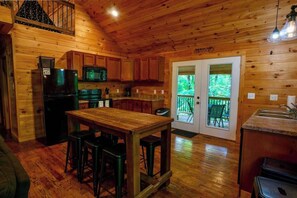 Ein Holzblock-Interieur mit Küche, Essbereich und einem Balkon mit Blick auf den Wald.