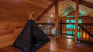 Interior em madeira com uma estrutura tipo tenda, piso de madeira e escada que leva a um andar superior.