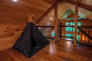 Ein Holzinnenraum mit einer zeltartigen Konstruktion, Holzboden und einer Treppe zu einer erhöhten Ebene.