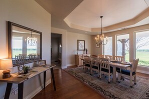 A dining area with a long table, chairs, a chandelier, and a view through large windows. - The Shiloh Ranch in Thrall (Thrall)