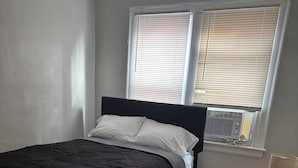A bedroom with a bed, a window with blinds, a radiator, and a small table with a tissue box. - Adorable 2-bedroom apartment with AC in cool Detroit (Detroit)