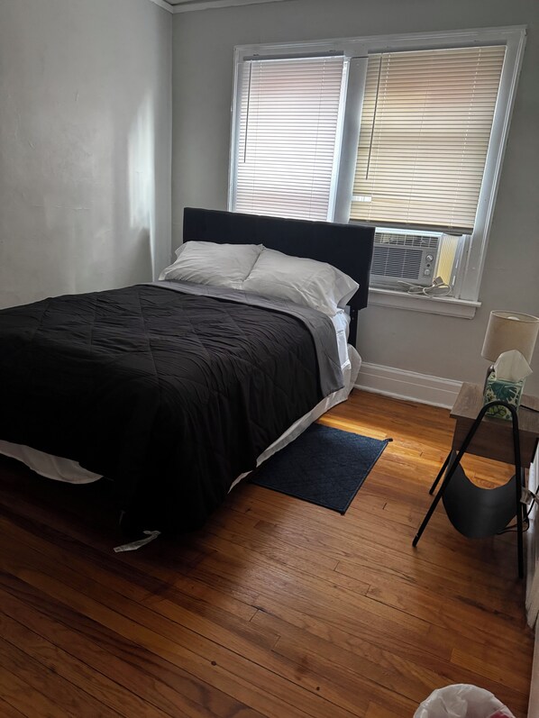 A bedroom with a bed, a window with blinds, a radiator, and a small table with a tissue box. - Adorable 2-bedroom apartment with AC in cool Detroit (Detroit)