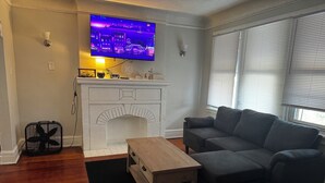 A living room with a fireplace, a flat-screen TV mounted above it, a grey sofa, and a wooden coffee table. - Adorable 2-bedroom apartment with AC in cool Detroit (Detroit)