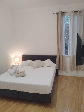 Una cama bien hecha con almohadas y una toalla doblada, una lámpara de noche y un televisor montado en la pared.