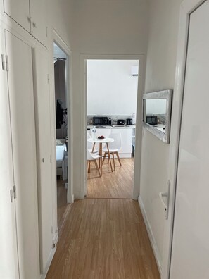 A hallway leading to a kitchen with white cabinets, a microwave, and a dining area with chairs and a table. - ☀️ Elegant 2-Bedroom Apartment – Cagnes-sur-Mer, Beach & Shopping on the Riviera (Cagnes-sur-Mer)
