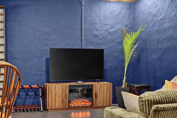A living room with a flat-screen TV on a wooden stand, a large potted plant, and a fireplace.