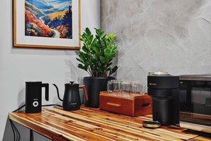 A kitchen area with a coffee maker, a kettle, a plant, and a framed picture on the wall.