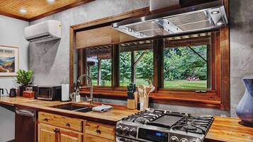 Une cuisine moderne équipée d’une cuisinière à gaz, de meubles en bois, d’une grande fenêtre donnant sur un espace verdoyant et d’un appareil de climatisation.