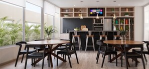 A modern dining area with round tables and chairs, a kitchen with a black backsplash, and a TV mounted above the counter. - Santa Isabel Santiago by Domus Travels (Santiago)