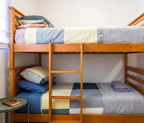 Ein Stockbett mit einer Leiter, ein kleiner Tisch mit Notizbuch und Stift sowie ein Fenster mit Jalousien.
