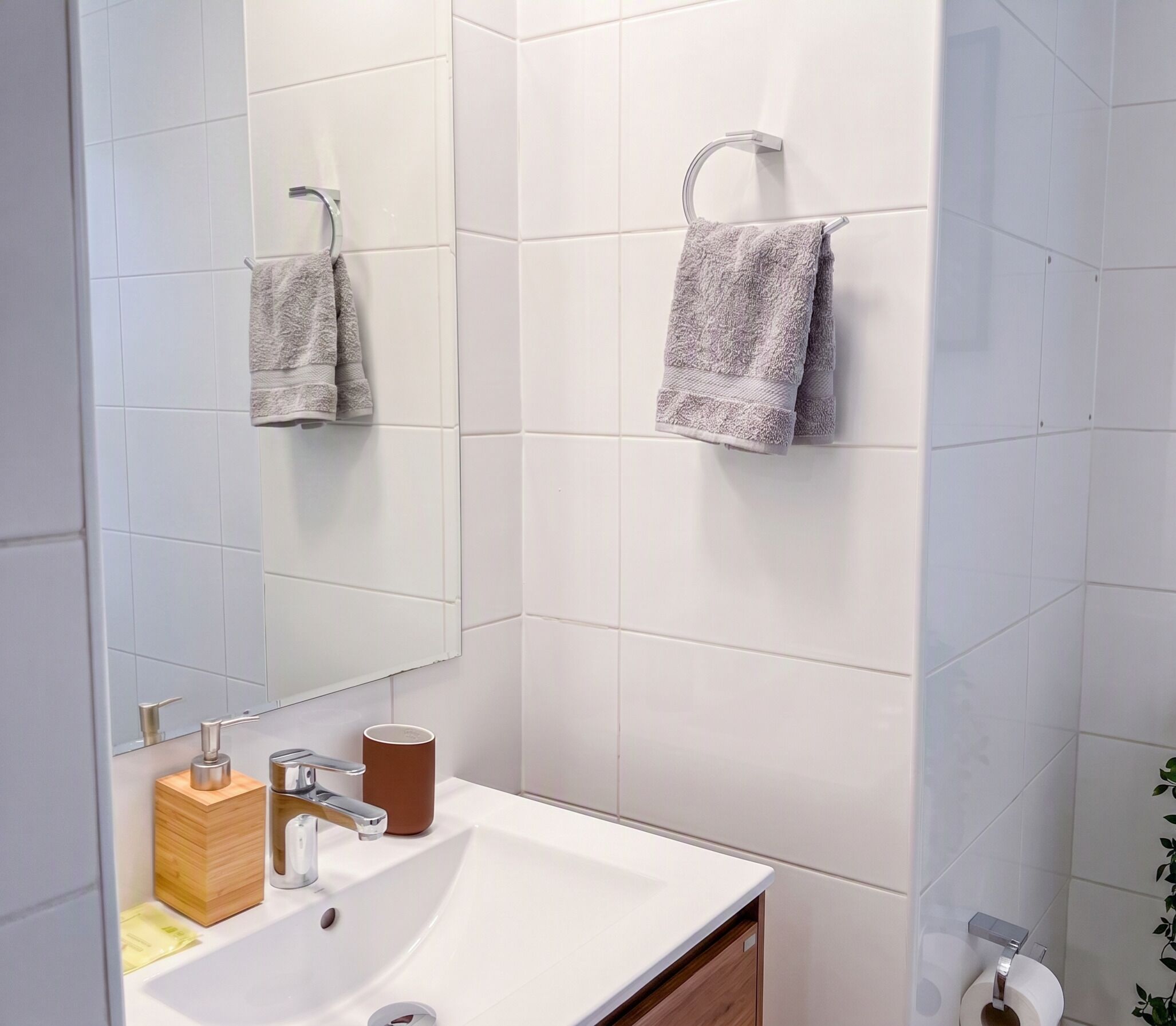 Un bagno con un lavandino bianco, uno specchio, due asciugamani, un dispenser per sapone e un portascirolettoni.